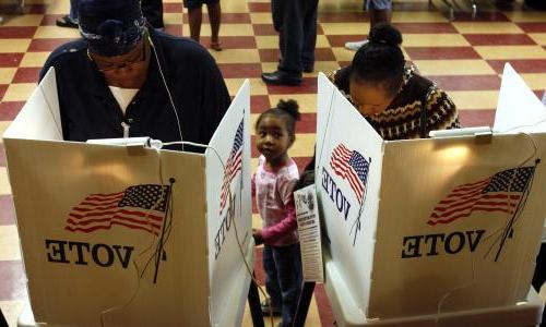 Two adults and a child stand in front of a voting booth